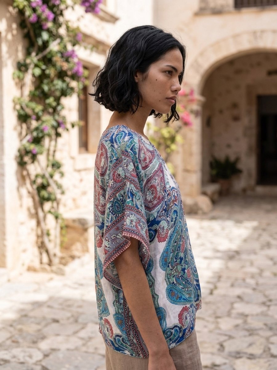 A woman in a silk scarf-print top in a stone courtyard